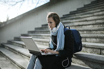 Student sits in stairwell, typing on laptop